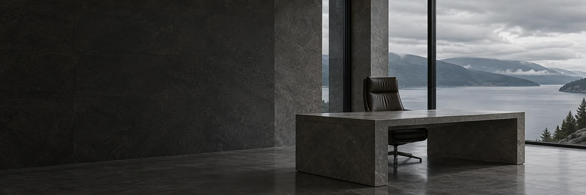 An empty stone office with a marble desk and leather chair, a lake and misted hills beyond the glass.